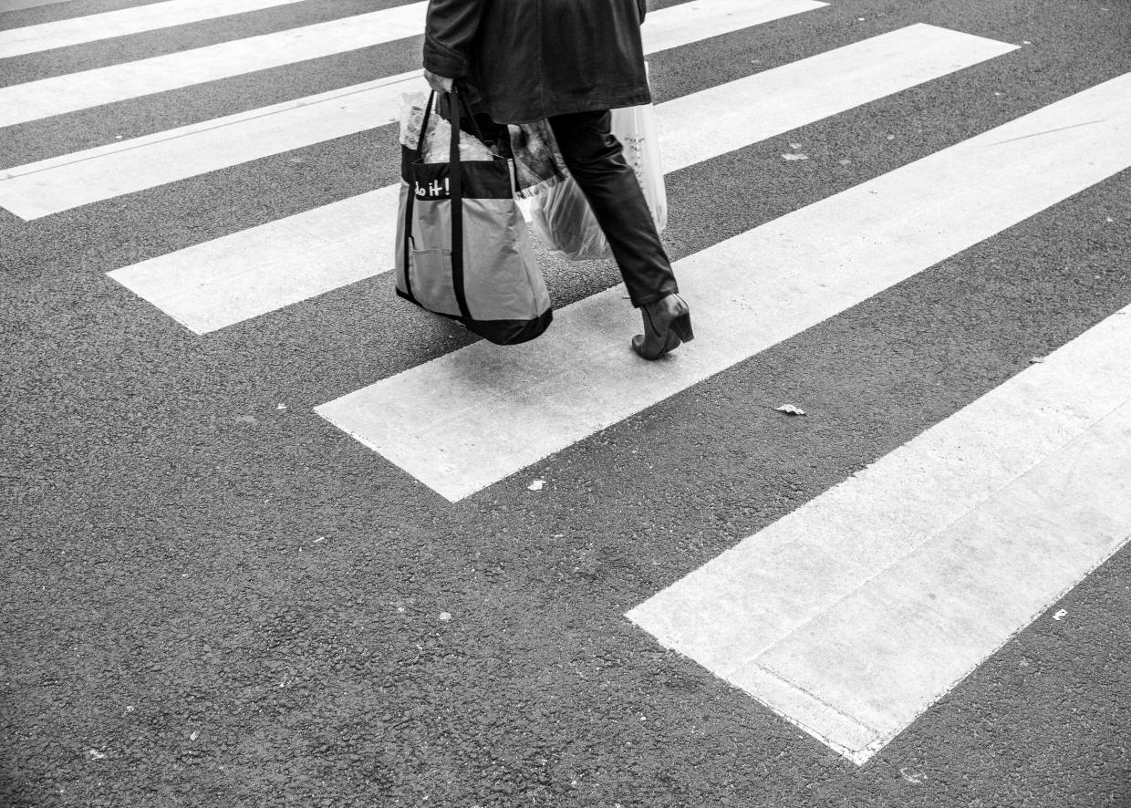 Eine Person mit zwei vollen Taschen läuft über einen Zebrastreifen.