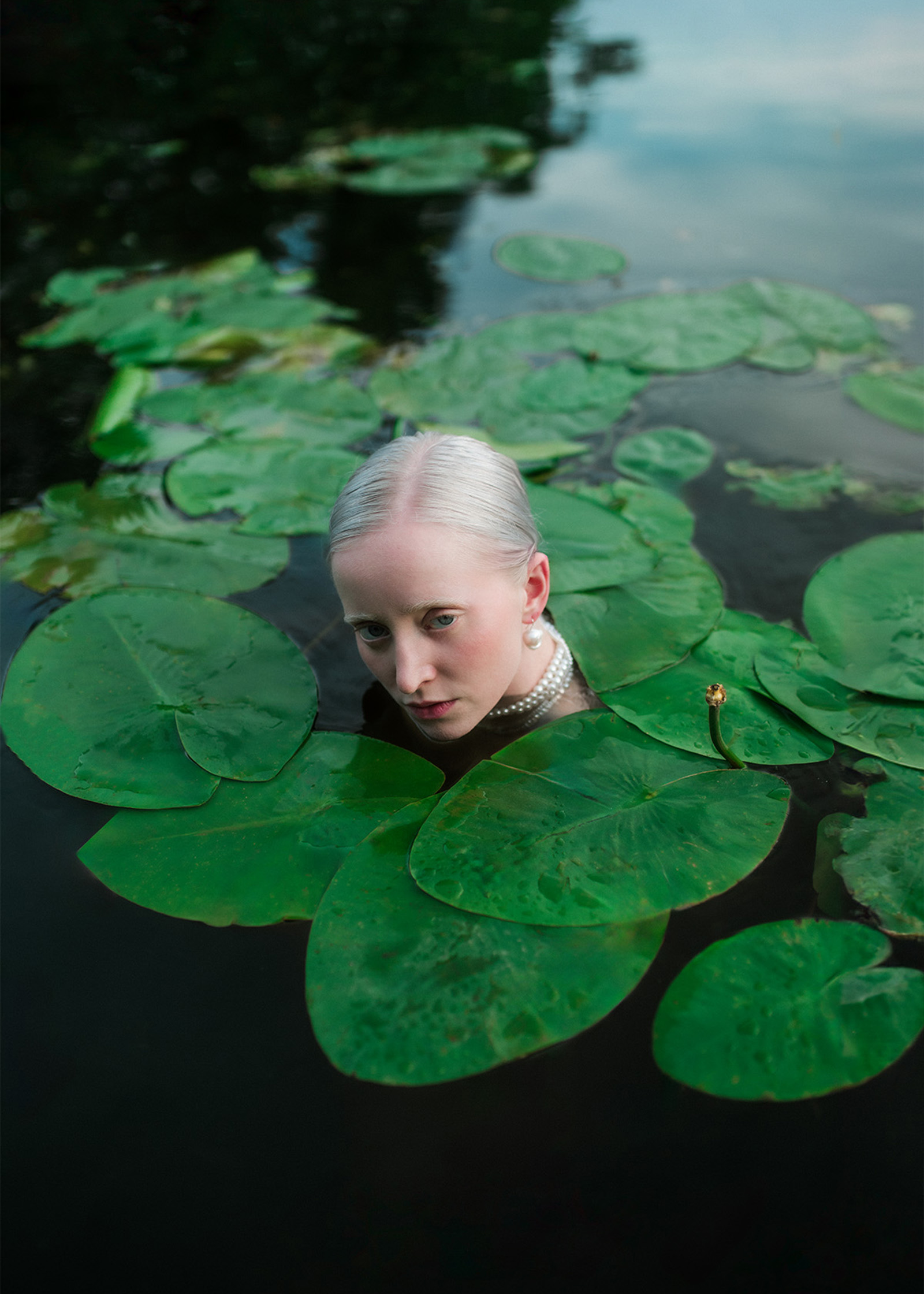 Eine Frau mit hellen Haaren steht bis zum Hals in einem See zwischen Seerosen.