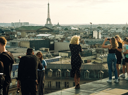 Im Vordergrund sieht man Touristen auf einem Ausschaupunkt, die die Skyline von Paris im Hintergrund fotografieren.