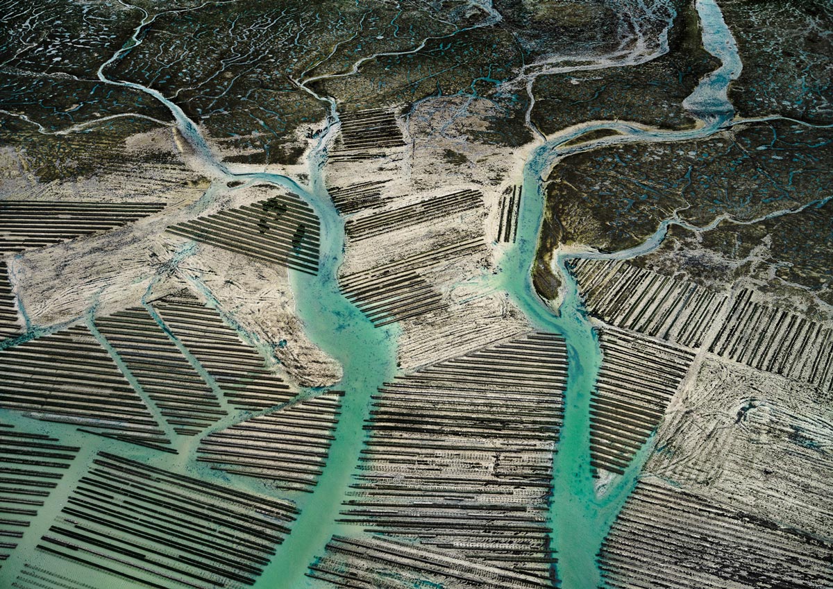 Ein Netzwerk von Salzbecken und Kanälen, die sich durch eine Küstenlandschaft schlängeln, mit klaren, geometrischen Mustern.