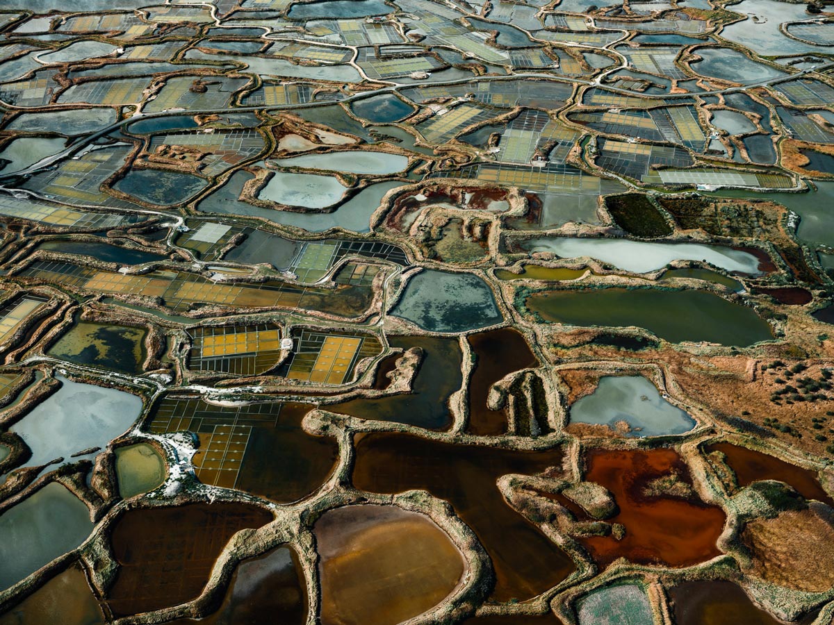 Eine Ansammlung von Salzbecken in verschiedenen Farben, die durch Dämme und Kanäle getrennt sind, mit einem geometrischen Muster, das sich über die Landschaft erstreckt.