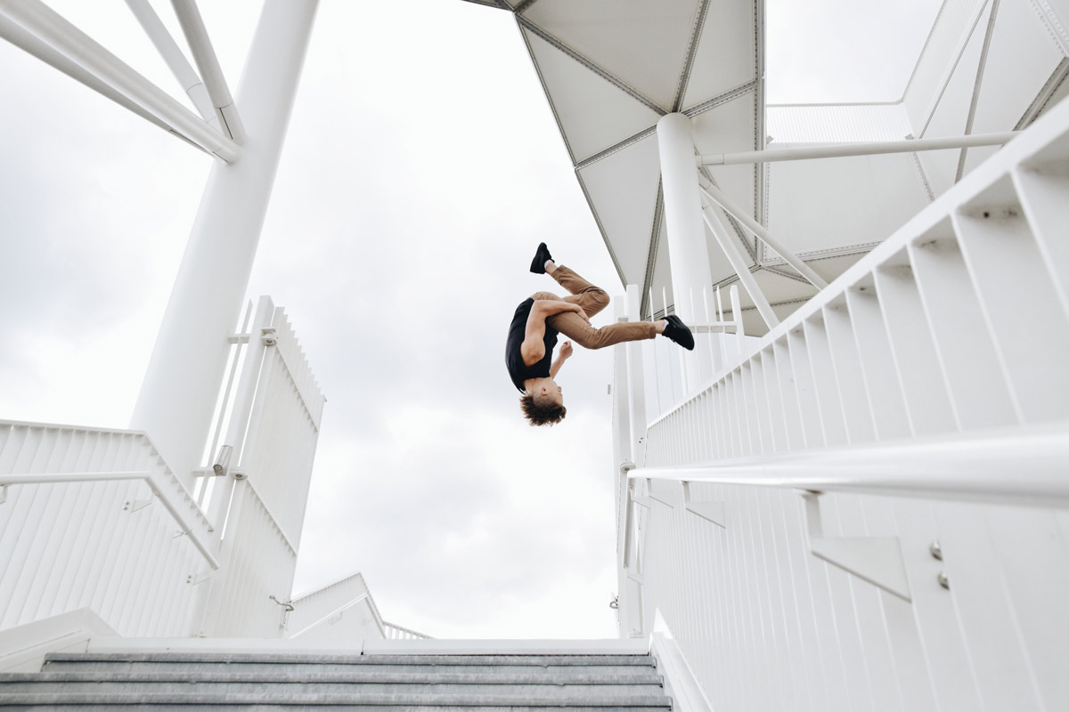 Ein Mann springt spektakulär von einem weißen Metallgeländer an einem modernen Gebäude.