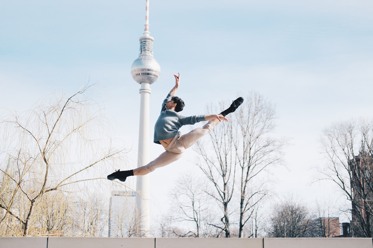 Ein Tänzer in grauer Kleidung springt vor dem Berliner Fernsehturm.