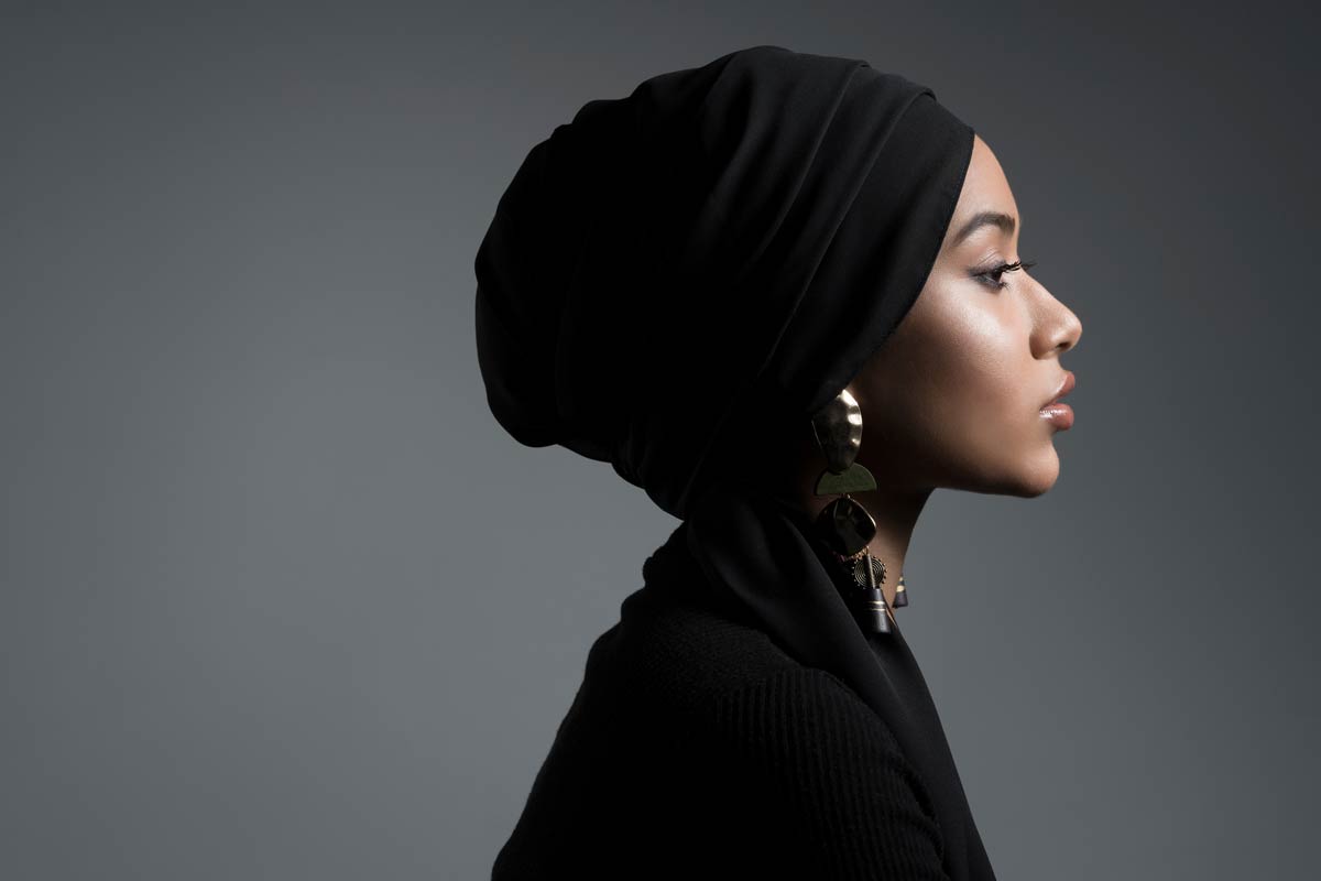 Seitenprofil einer Frau mit einem schwarzem Kopftuch und großen Ohrringen.