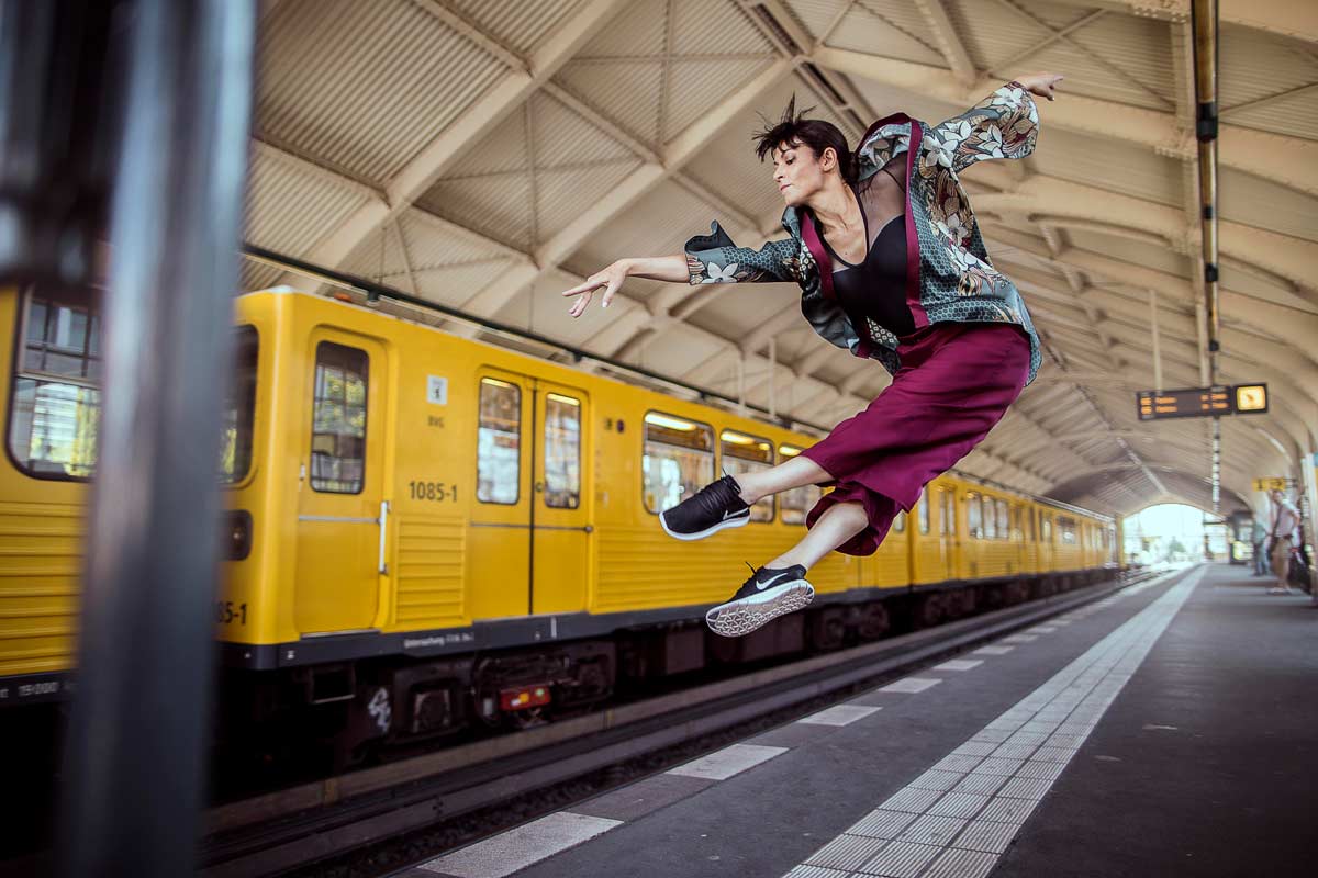 Eine Frau in einem bunten Outfit springt in einem U-Bahnhof.