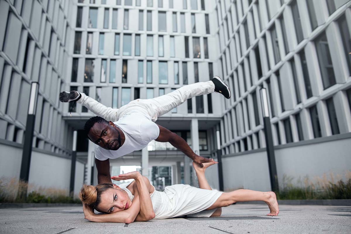 Ein Mann und eine Frau in weißer Kleidung balancieren in einer urbanen Umgebung.