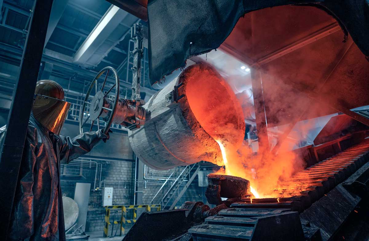 Ein Arbeiter in einer Gießerei bedient eine Maschine, die glühendes Metall in Formen gießt.