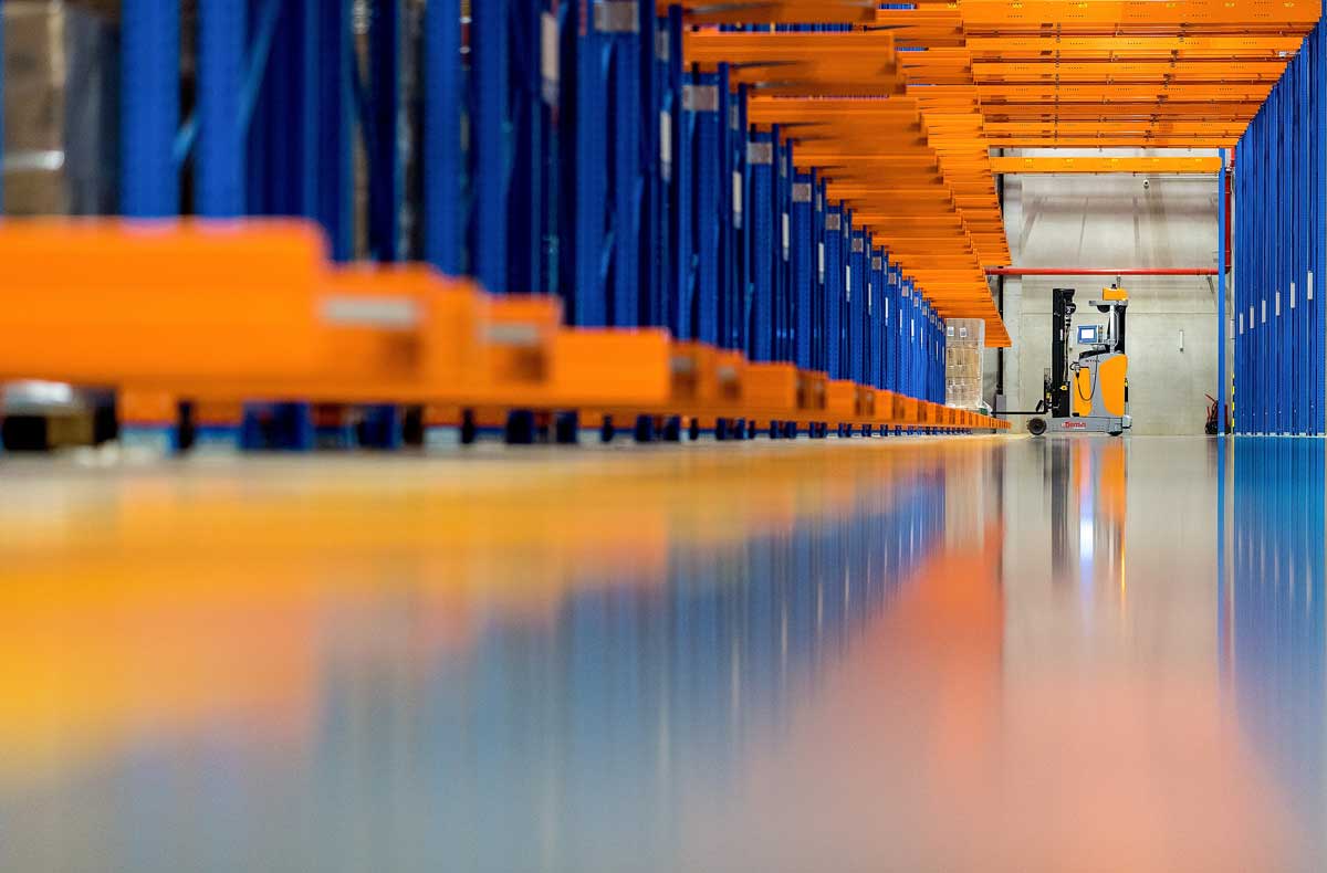 Ein automatisiertes Lager mit Regalen und einem Gabelstapler, der Paletten bewegt.