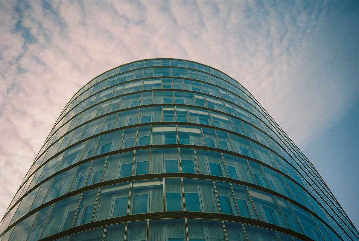 Ein modernes Glasgebäude, dessen gläserne Front sich rund vor dem blauen Himmel absetzt.