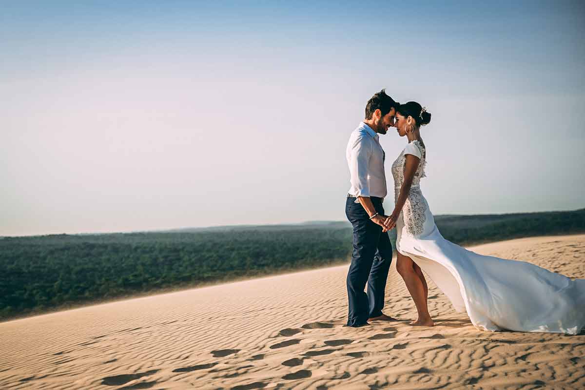 Ein Hochzeitspaar in einer intimen Pose auf einer Sanddüne vor dem blauen Meer.