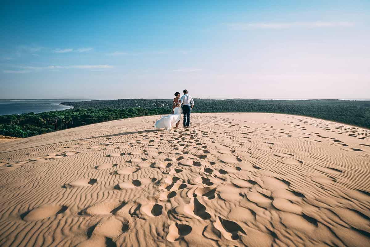 Ein Paar geht Hand in Hand über eine Sanddüne.