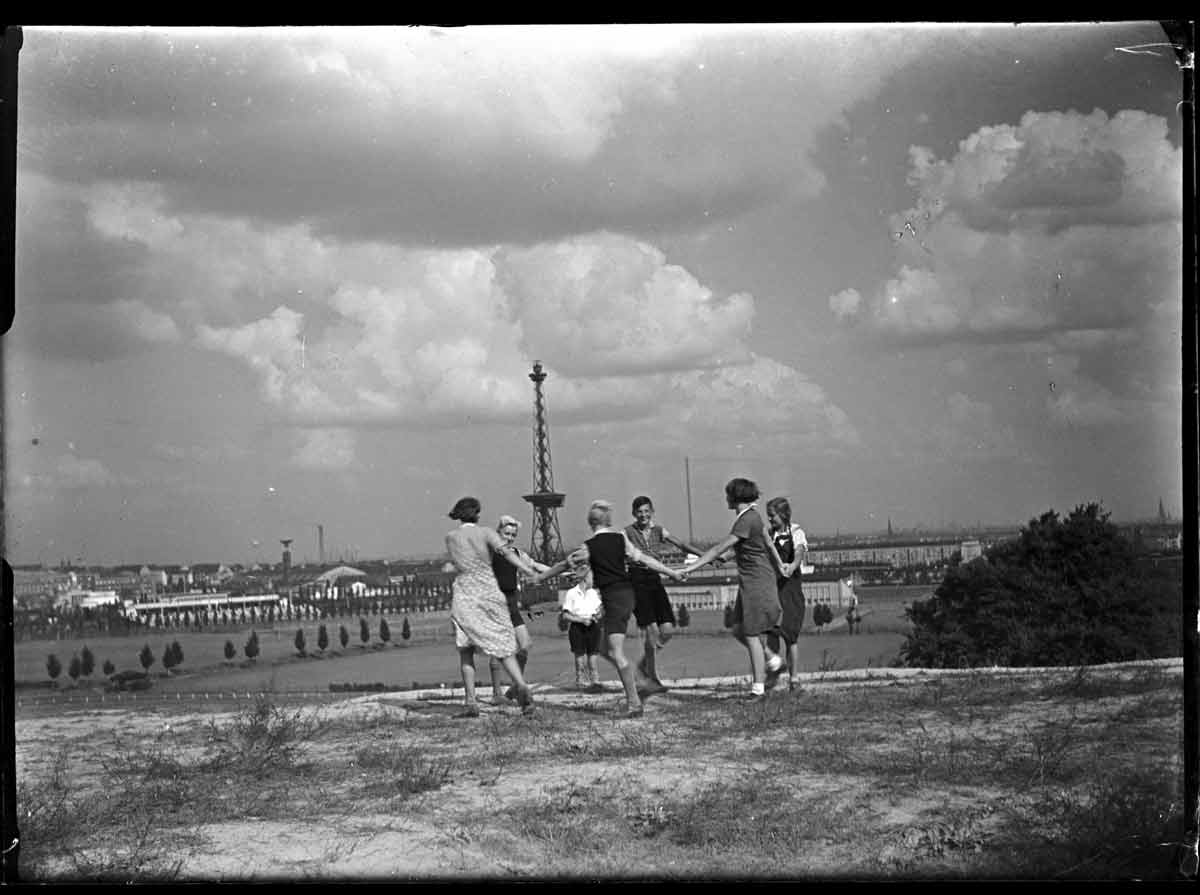 Eine Gruppe von Menschen tanzt im Freien auf einem Hügel mit Blick auf Berlin und dem Fernsehturm im Hintergrund.