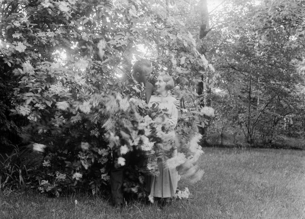 Ein Paar steht unter einem großen Baum und umarmt sich, während sie in die Kamera lächeln.