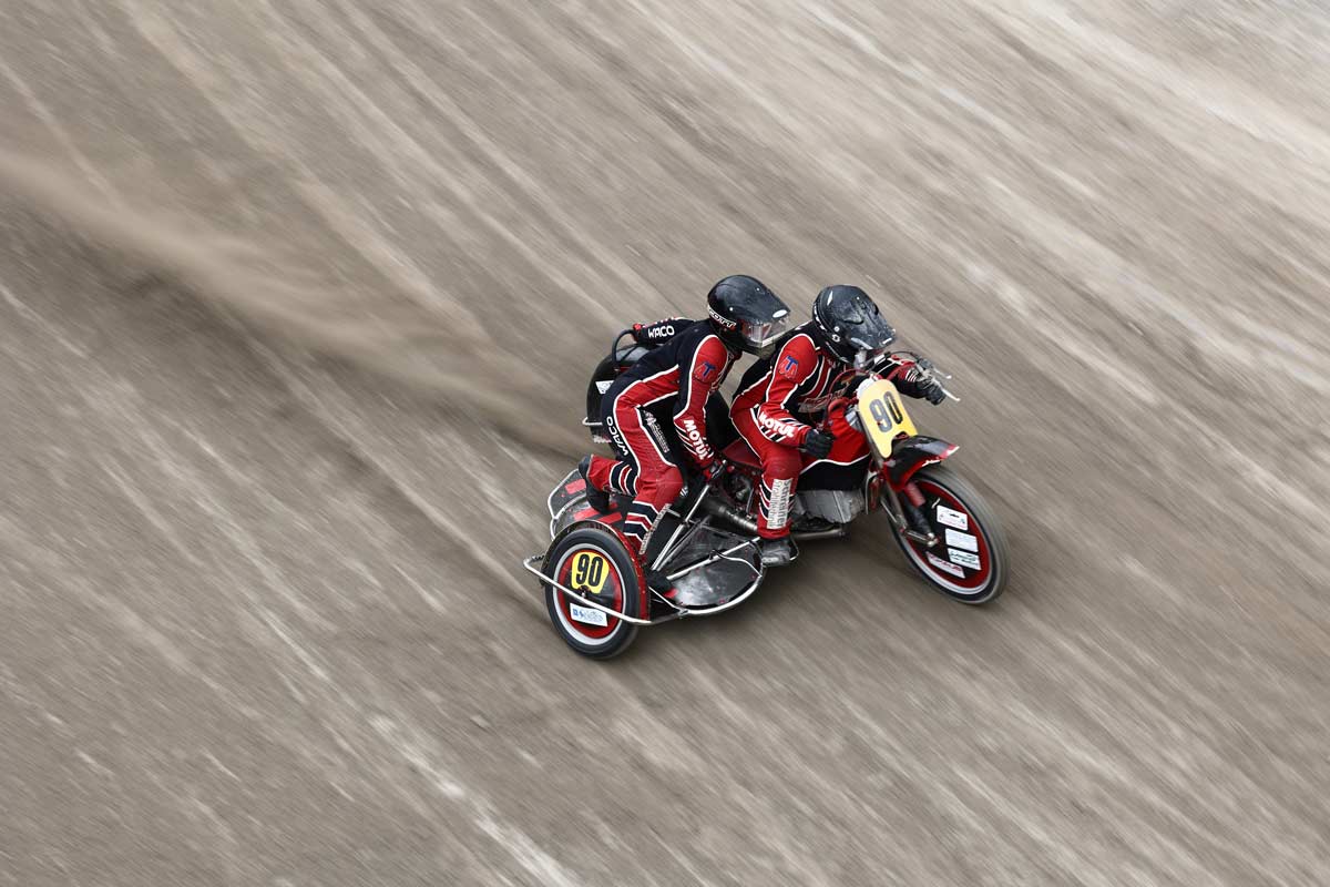 Zwei Rennfahrer auf einem, sich schnell bewegenden, Dreirad.