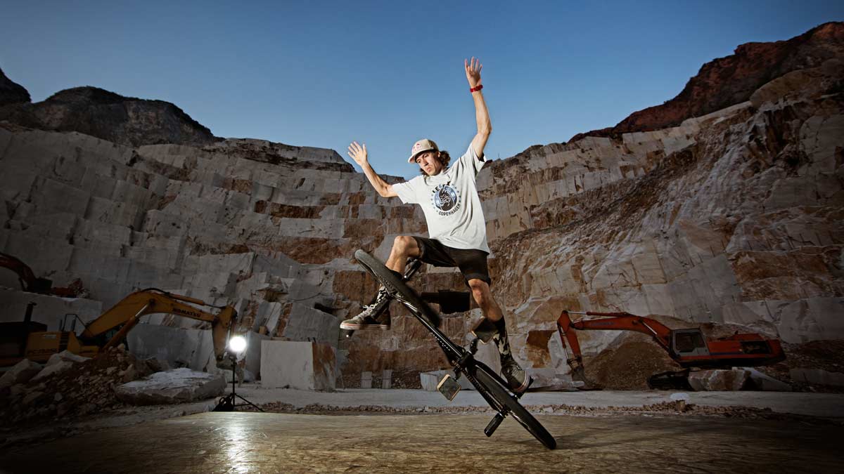 Ein BMX Fahrer balanciert auf seinem Fahrrad in einem schwach beleuchtetem Steinbruch.