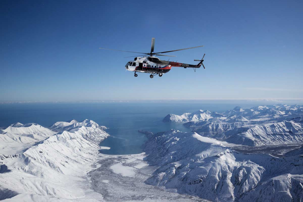 Ein Helikopter in der Luft über einer schneebedeckten Berglandschaft.